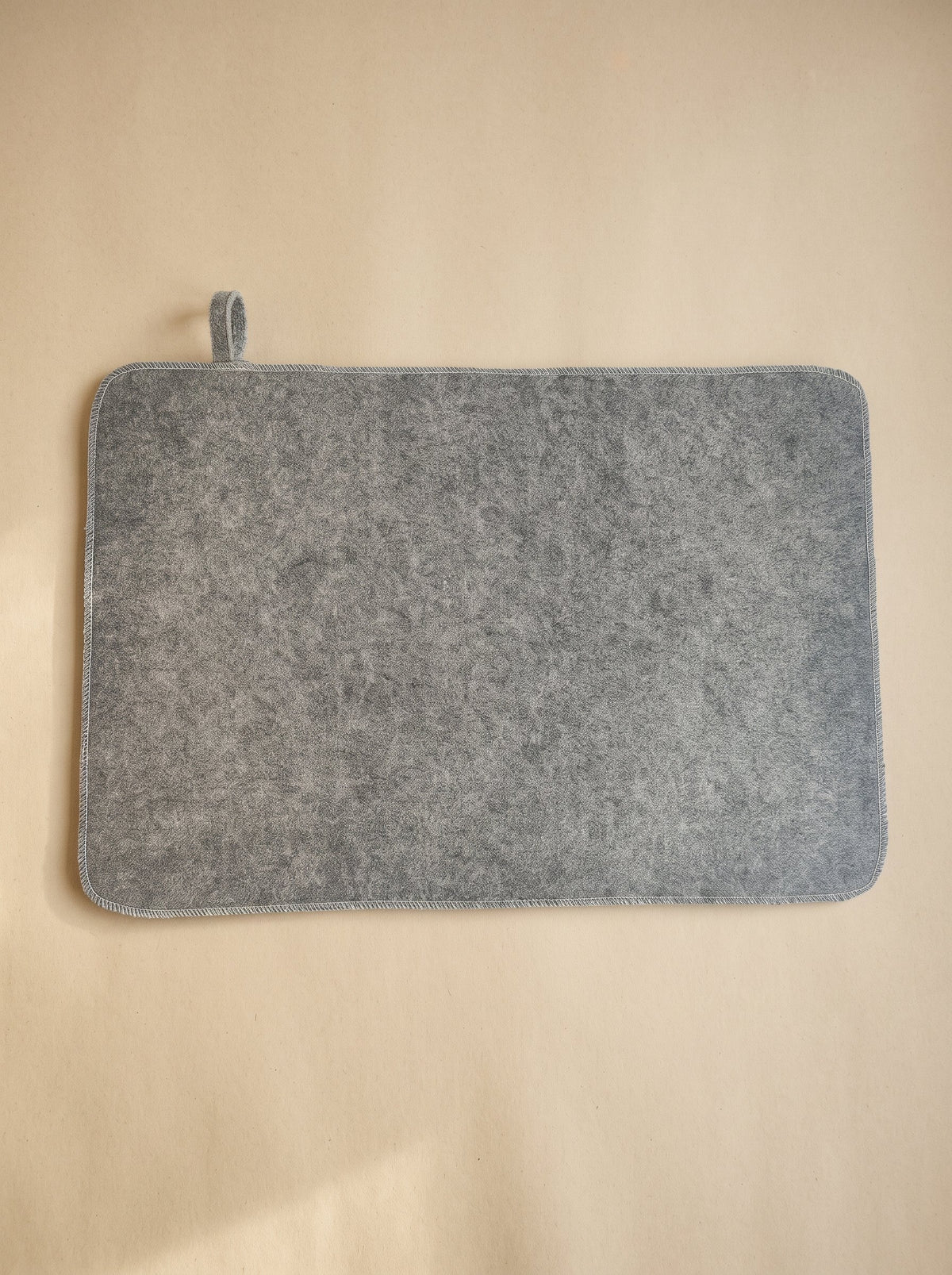 P1-gri | Gray felt sauna seat pad with a hanging loop, on an oat background